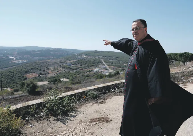 L’archevêque maronite de Tyr, Monseigneur Abdallah, montre la frontière avec Israël, située au sommet de la colline visible au loin. ©Gaby Leygues