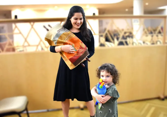 Une femme juive orthodoxe tient un rouleau de la Torah tandis que sa fille embrasse un jouet de la Torah. RNS