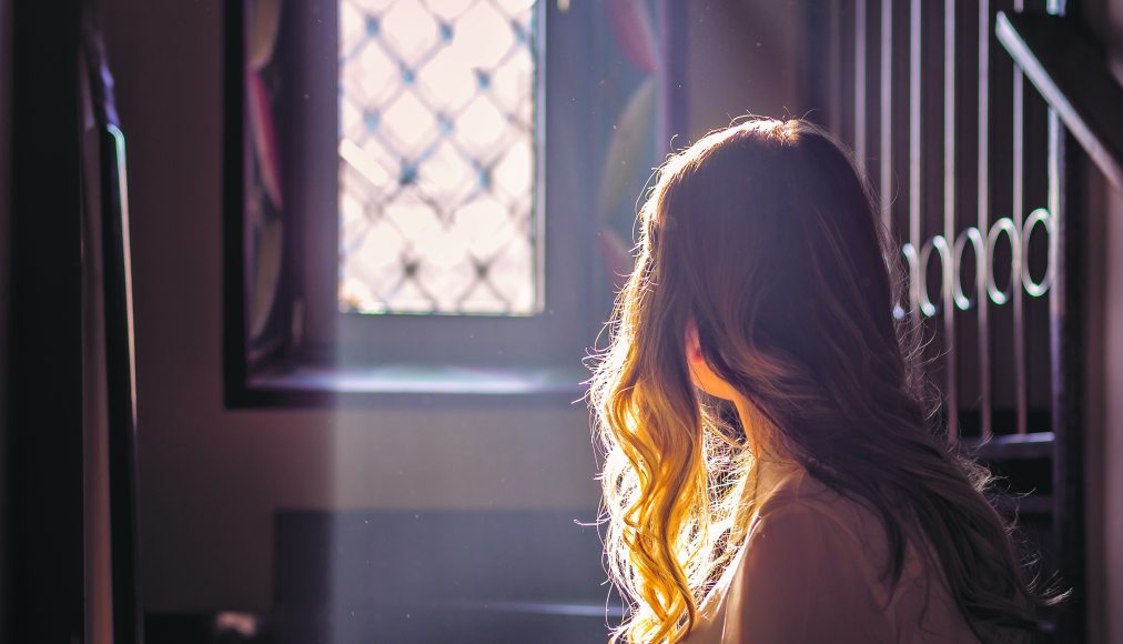 Jeune adolescente regardant par la vitre d&#039;une église. / © iStock