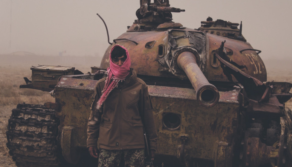 Août 2021, dans un faubourg de Kaboul (Afghanistan), un homme armé pose devant une épave de tank taliban. / ©iStock/Trent Inness