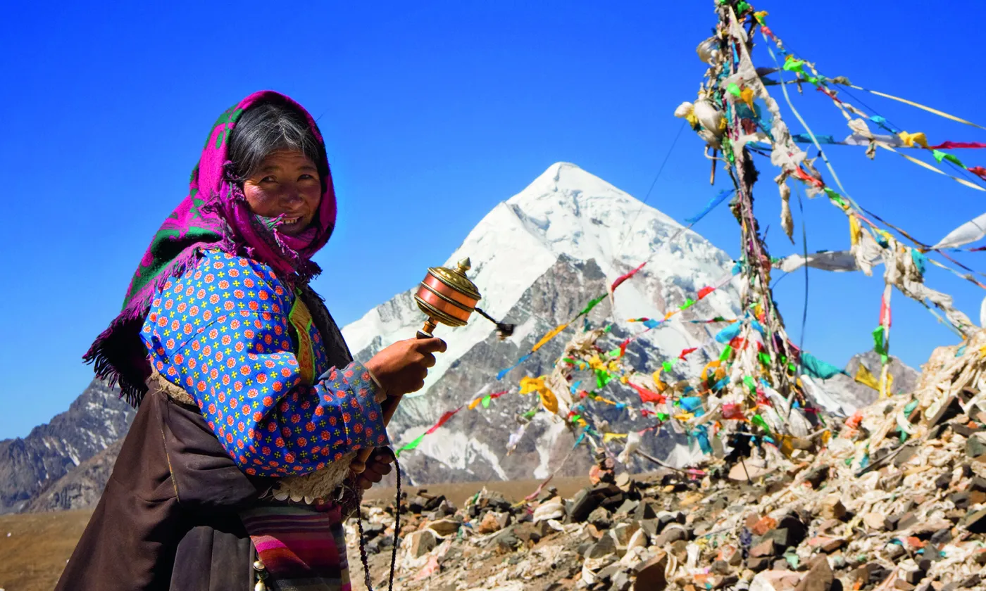 Moulin à prières dans la main, une pèlerine bouddhiste s’est arrêtée devant les petits drapeaux sur lesquels les Tibétains écrivent des invocations que le vent emporte vers les divinités. © Christopher Tozer/Alamy Stock Photo