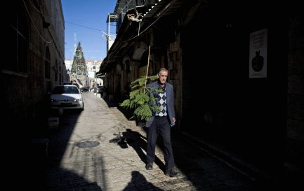 Un Palestinien portant un sapin de Noël dans une rue pavée de la vieille-ville de Jérusalem. / Keystone/ Abir Sultan